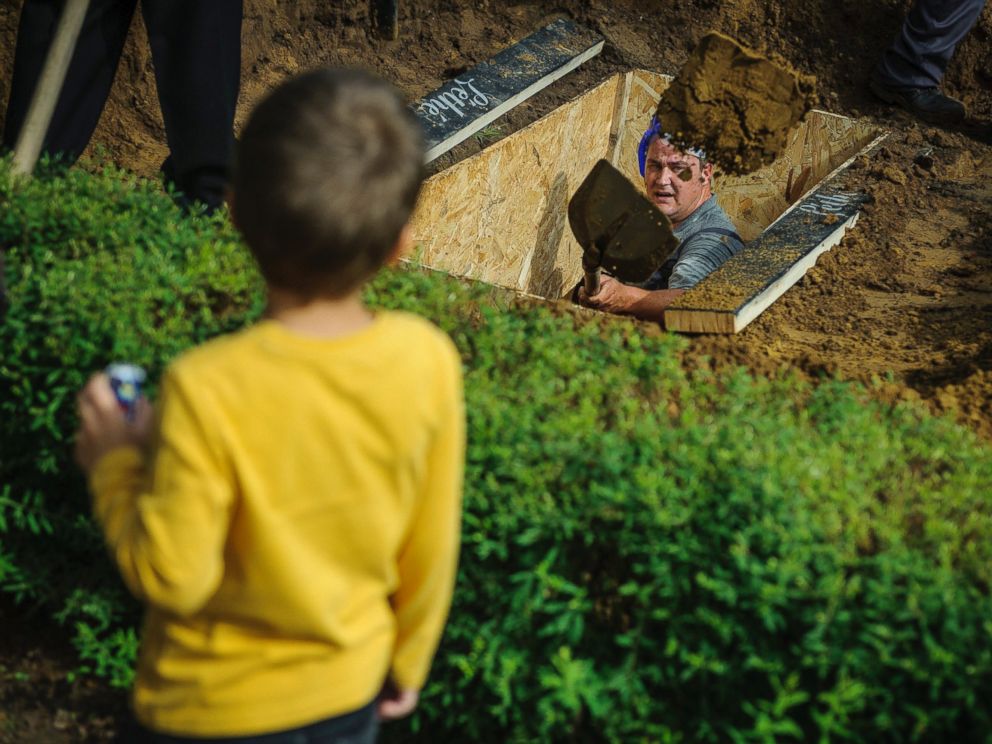 PHOTO: A gravedigger competes while a boy looks on during the first National Grave Digging competition at the public cemetery of Debrecen, Hungary, June 3, 2016.
