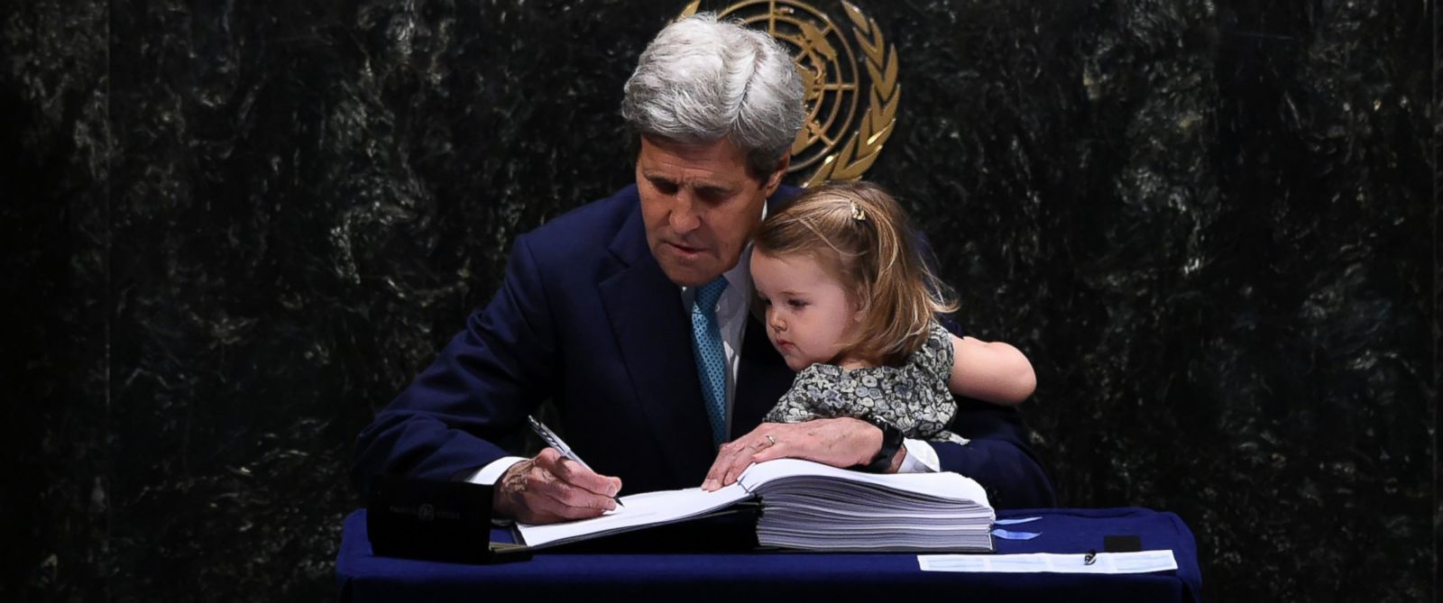 PHOTO: Secretary of State John Kerry signs the Paris Agreement at the United Nations General Assembly Hall while holding his granddaughter, Isabelle Dobbs-Higginson, April 22, 2016, in New York.